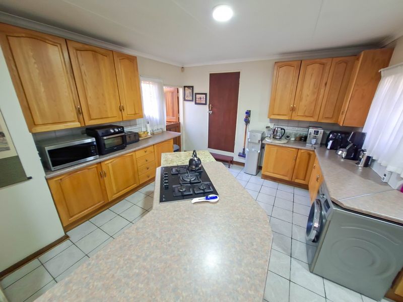 A functional kitchen featuring wooden cabinetry, laminate countertops, a central island with a gas hob, and tiled flooring.