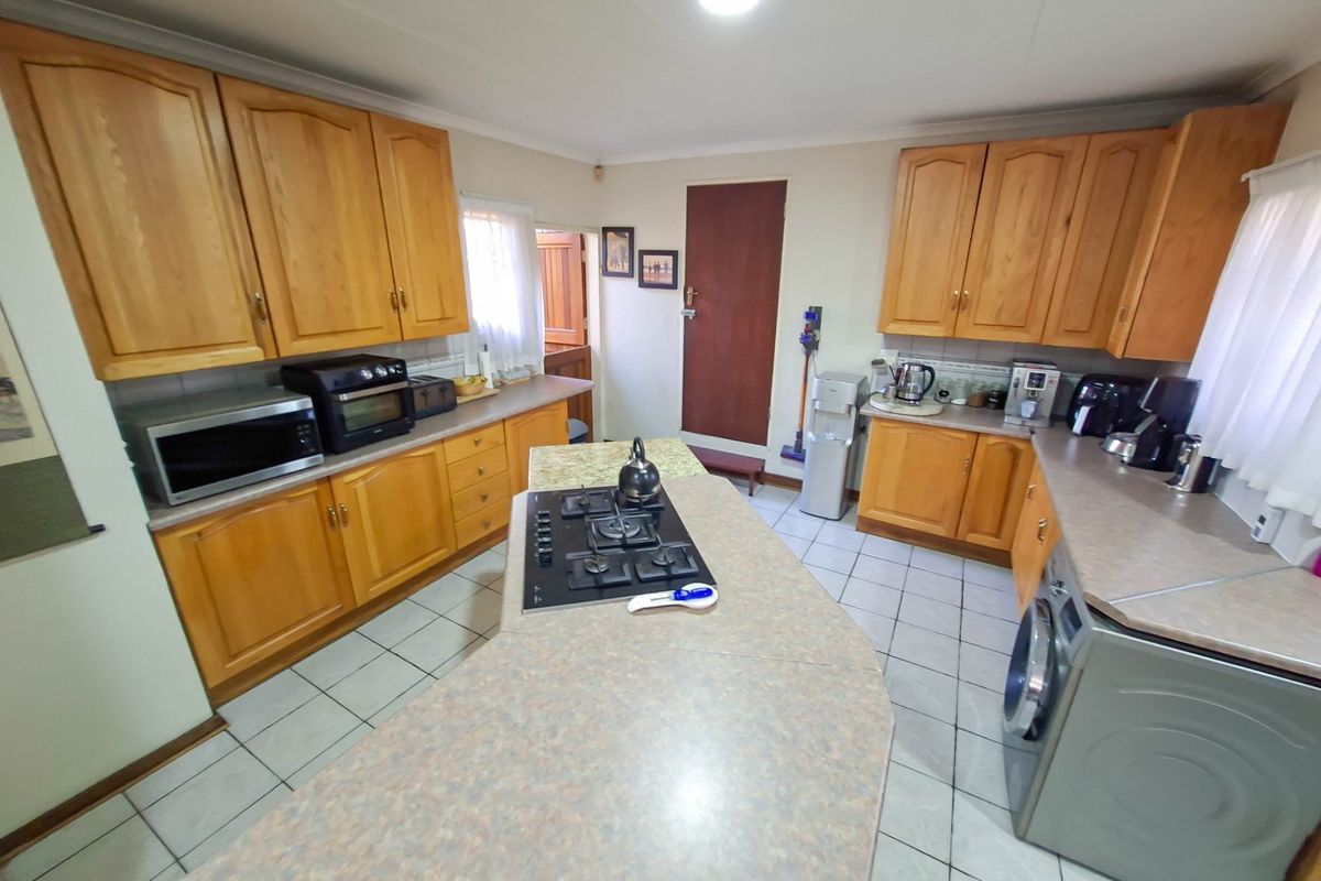 A functional kitchen featuring wooden cabinetry, laminate countertops, a central island with a gas hob, and tiled flooring.