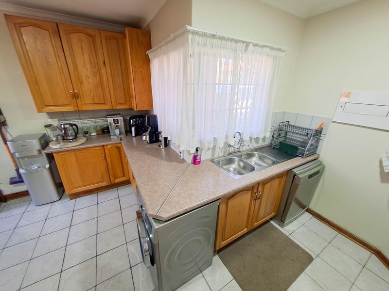 A functional kitchen featuring wooden cabinetry, laminate countertops, a double bowl stainless steel sink, and tiled flooring.