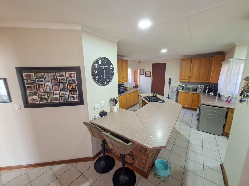 A functional kitchen featuring wooden cabinetry, a breakfast bar with a brick base, gas hob, and tiled flooring throughout.