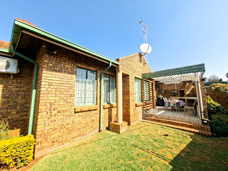 Rear exterior view of the townhouse featuring a face brick facade, a covered patio with a built-in braai, and a small private garden area.