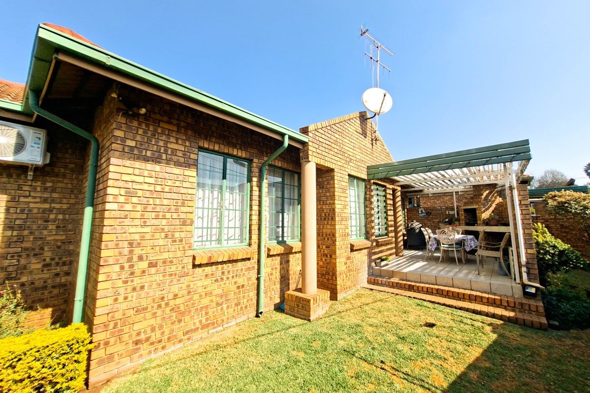 Rear exterior view of the townhouse featuring a face brick facade, a covered patio with a built-in braai, and a small private garden area.