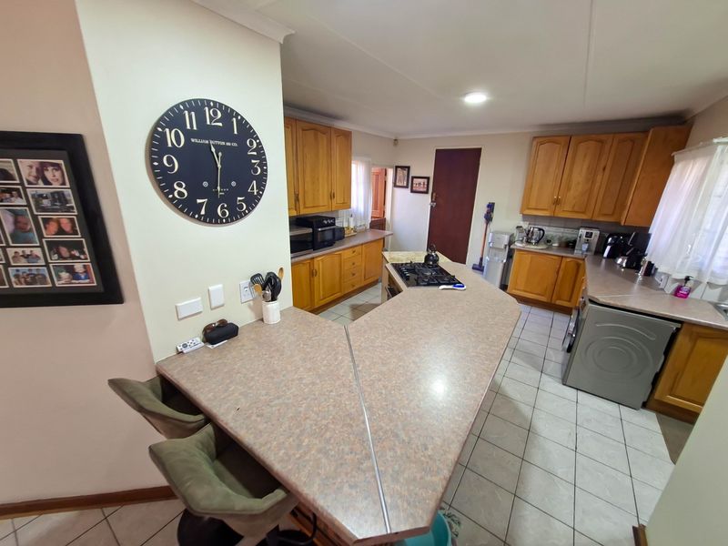 A functional kitchen featuring wooden cabinetry, laminate countertops, a central breakfast bar with a gas hob, and tiled flooring.