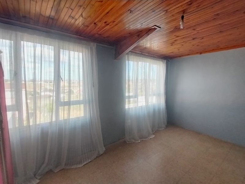 An empty bedroom featuring a timber-clad ceiling with an exposed beam, tiled flooring, and large windows providing natural light.