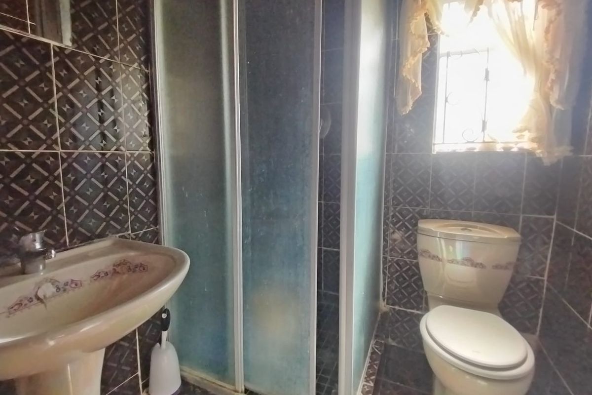 A compact bathroom featuring a pedestal basin, a shower enclosure, and a toilet, finished with dark patterned wall and floor tiles.