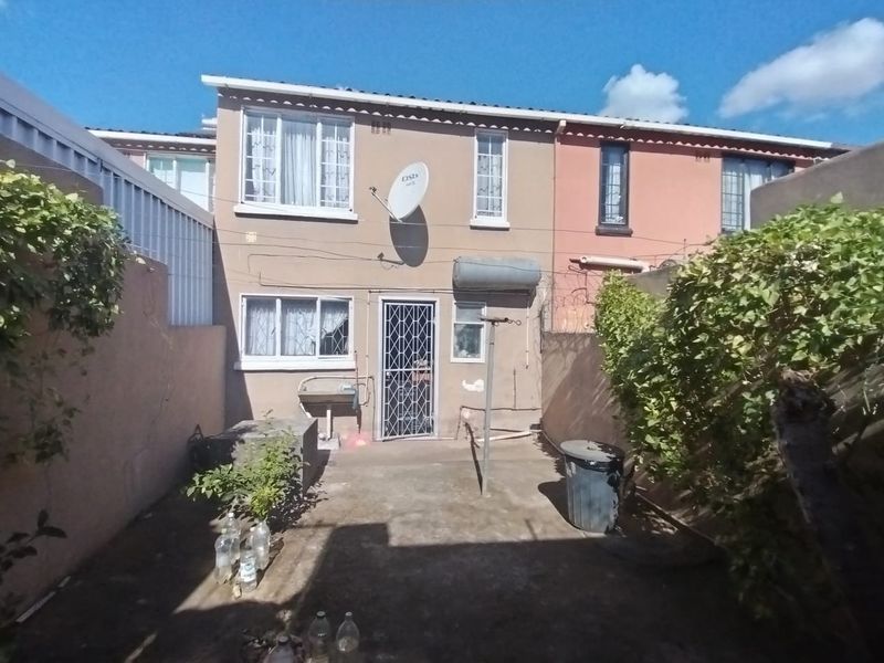 Rear view of the property featuring a concrete patio, security gate, external wash basin, and perimeter wall with security fencing.