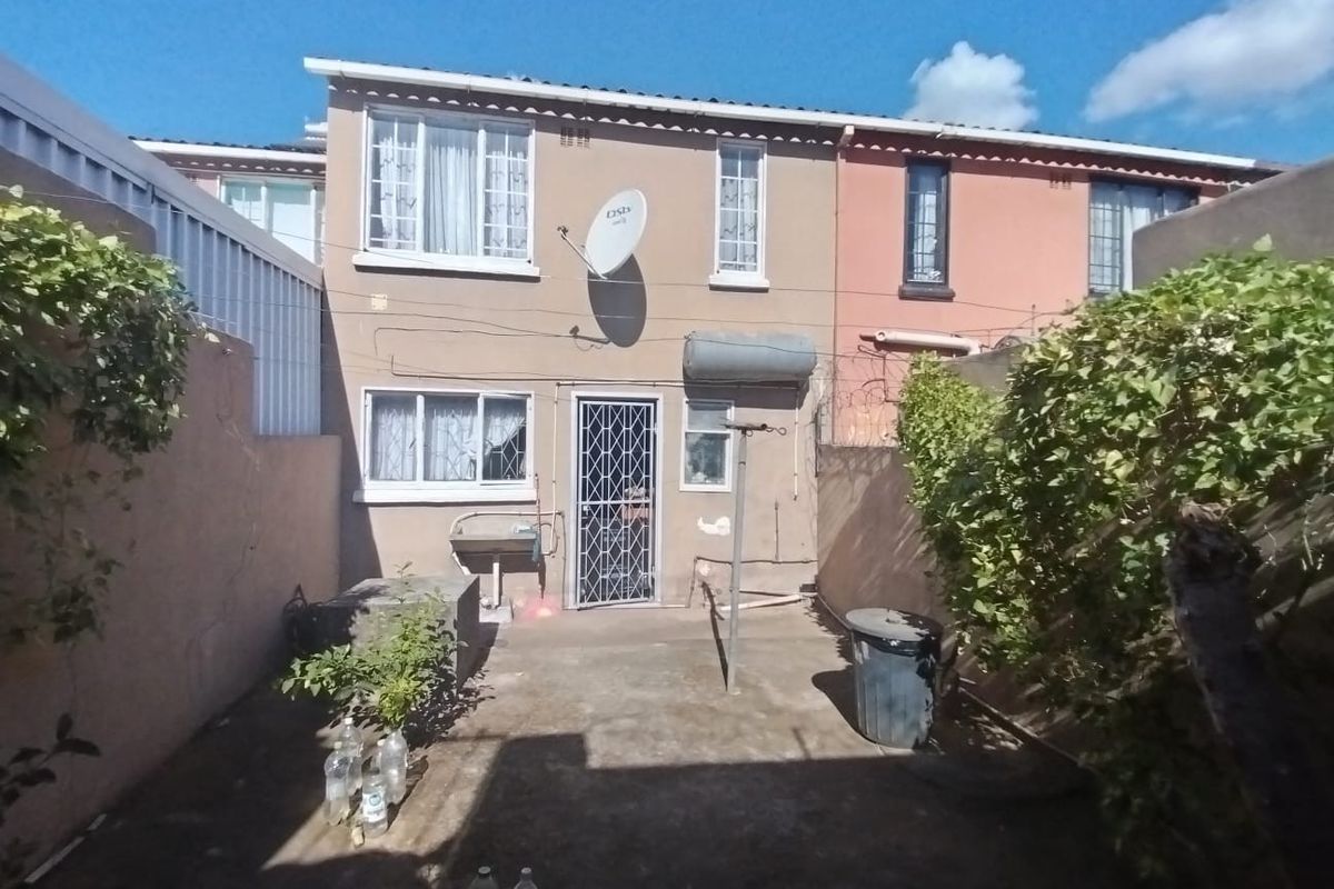 Rear view of the property featuring a concrete patio, security gate, external wash basin, and perimeter wall with security fencing.