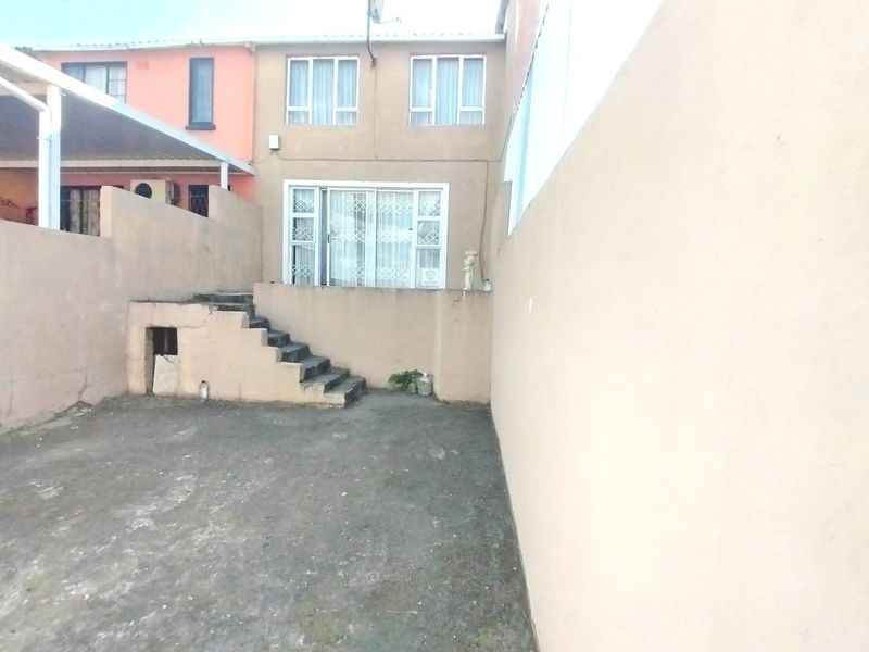Rear exterior view of the property featuring a paved courtyard, concrete stairs leading to a sliding glass door, and boundary walls.
