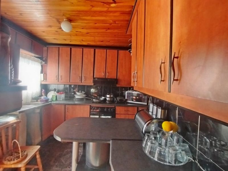 A functional kitchen featuring extensive wooden cabinetry, dark laminate countertops, a built-in oven with extractor fan, and a timber-clad ceiling.
