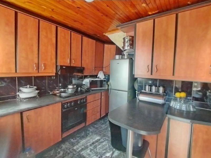 A functional kitchen featuring timber ceiling paneling, laminate cabinetry, built-in oven, and dark tiled backsplash, offering potential for a modern cosmetic update.