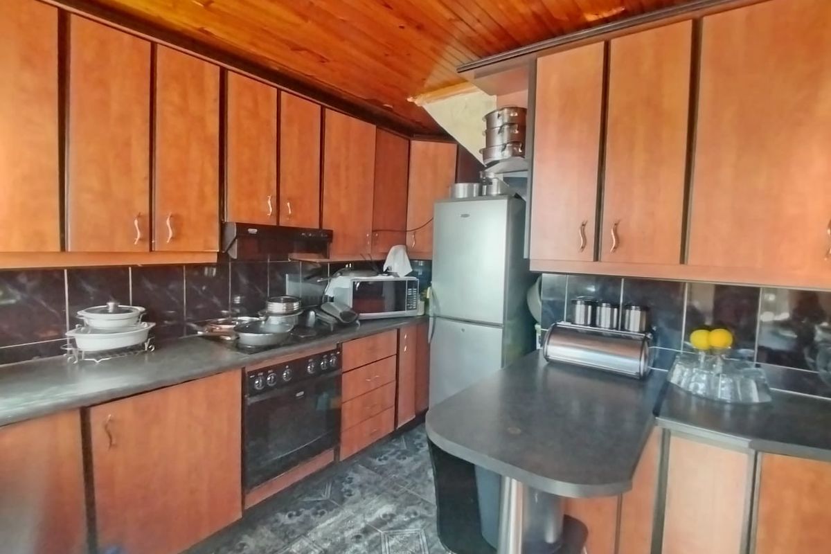 A functional kitchen featuring timber ceiling paneling, laminate cabinetry, built-in oven, and dark tiled backsplash, offering potential for a modern cosmetic update.