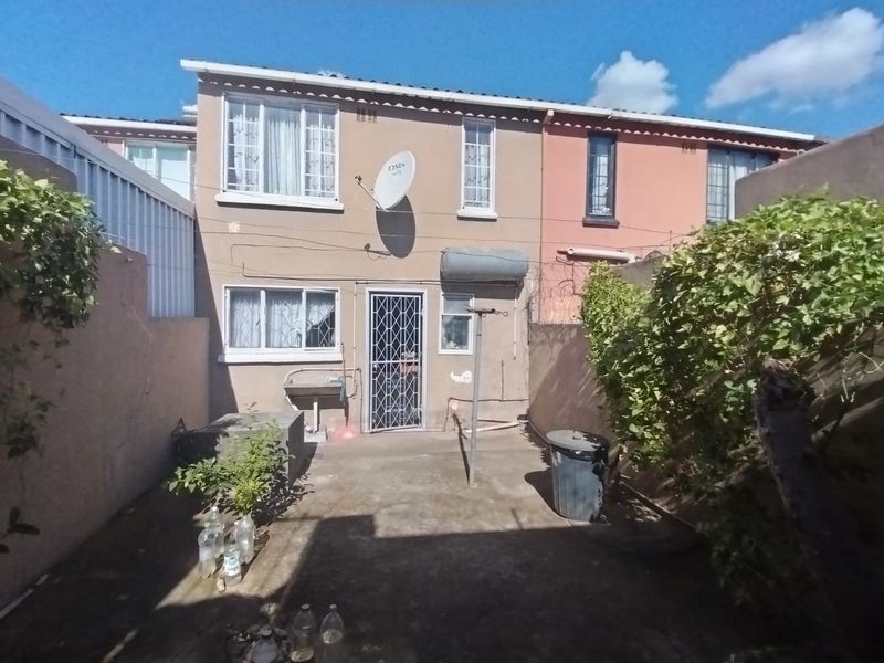 Rear exterior view of the property featuring a concrete patio, security gate, external wash basin, and wall-mounted satellite dish.