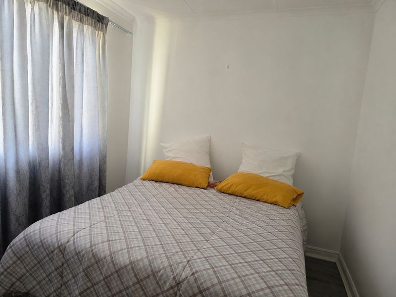 A simple bedroom featuring neutral walls, grey wood-look flooring, and a window with installed curtain rails.
