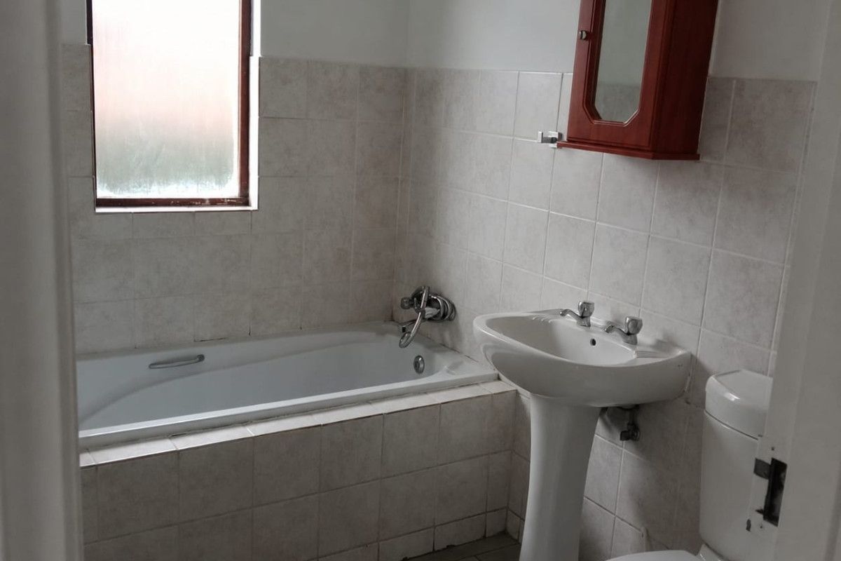 A functional bathroom featuring a bathtub, pedestal basin, toilet, and neutral wall tiling, offering a clean and practical space.