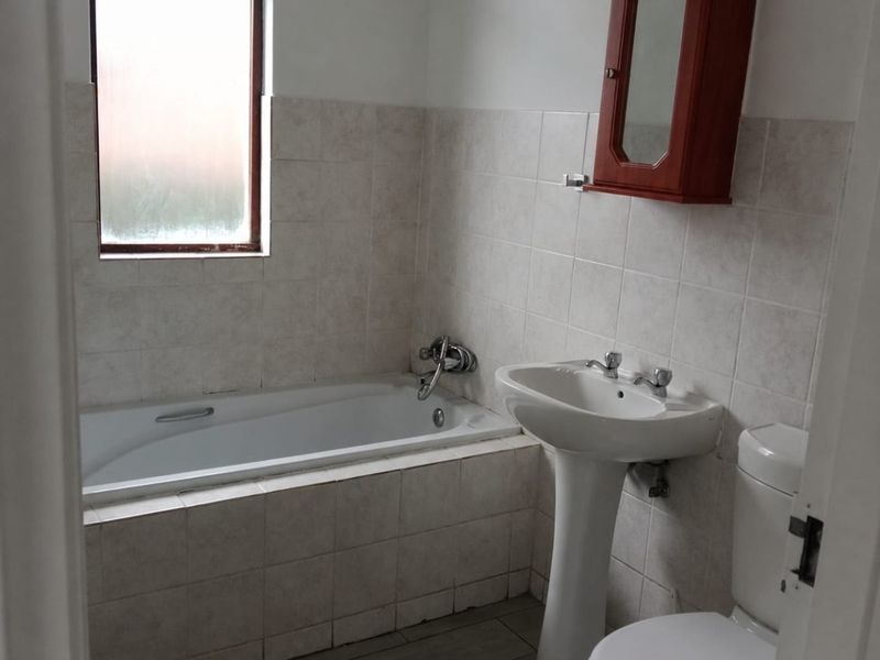 A functional bathroom featuring a bathtub, pedestal basin, toilet, and neutral wall tiling, offering a clean and practical space.