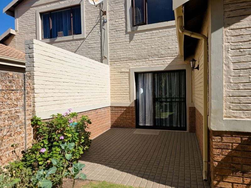 A private paved patio area featuring a sliding glass door entrance, brick boundary wall, and exterior lighting, providing a functional outdoor space.