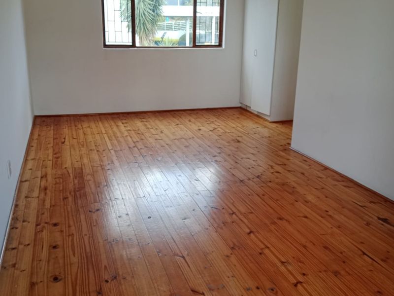 An empty bedroom featuring polished timber flooring, a built-in wardrobe, and a window fitted with security bars.