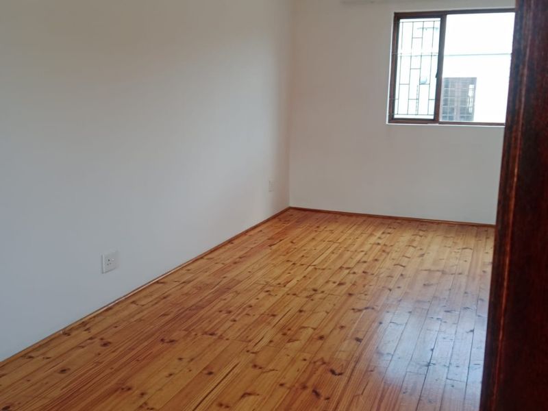 A bright, empty bedroom featuring polished timber flooring and a window fitted with security bars.