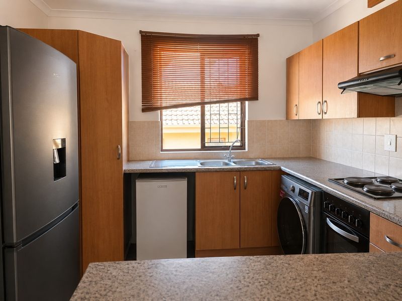Functional kitchen featuring wood-finish cabinetry, granite-look countertops, built-in oven with hob, and a double sink with window view.