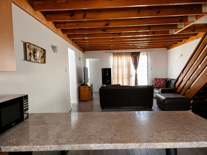 Open plan living area featuring exposed timber ceiling beams, a granite kitchen breakfast bar, and a timber staircase leading to the upper level.