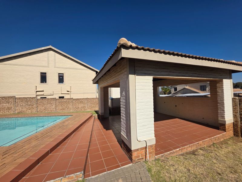 Outdoor pool area featuring a covered patio with tiled flooring, brick pillars, and a swimming pool set within a secure townhouse complex.