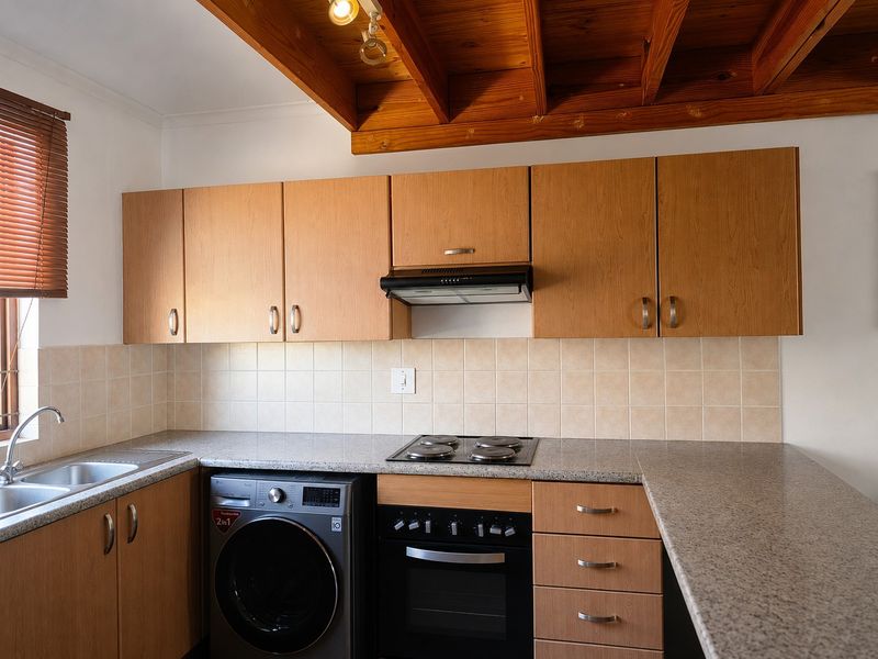 Functional kitchen featuring wood-finish cabinetry, granite-look countertops, tiled splashbacks, built-in oven and hob, and distinctive exposed timber ceiling beams.