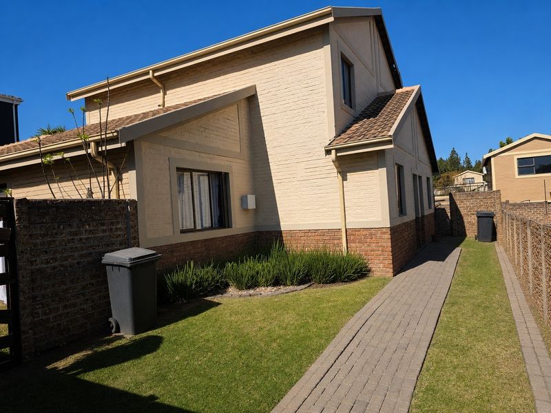 Rear view of a two-story townhouse featuring a brick facade, tiled roof, paved walkway, and a well-maintained lawn area.