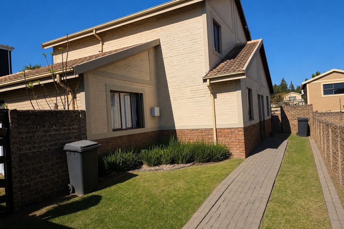 Rear view of a two-story townhouse featuring a brick facade, tiled roof, paved walkway, and a well-maintained lawn area.