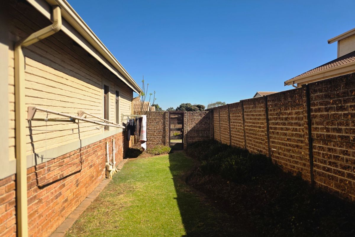 A side garden area featuring a lawn, brick boundary wall, and timber gate access, providing a private outdoor space for the townhouse.