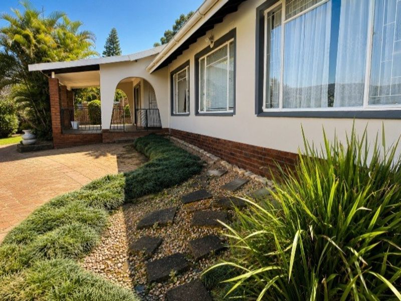 Rear exterior view featuring a covered patio, brick base detailing, and a landscaped garden with a stone pathway leading to the home.