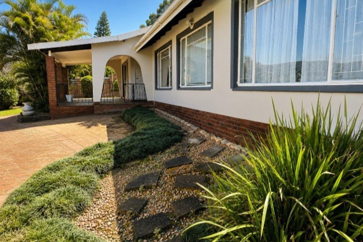 Rear exterior view featuring a covered patio, brick base detailing, and a landscaped garden with a stone pathway leading to the home.