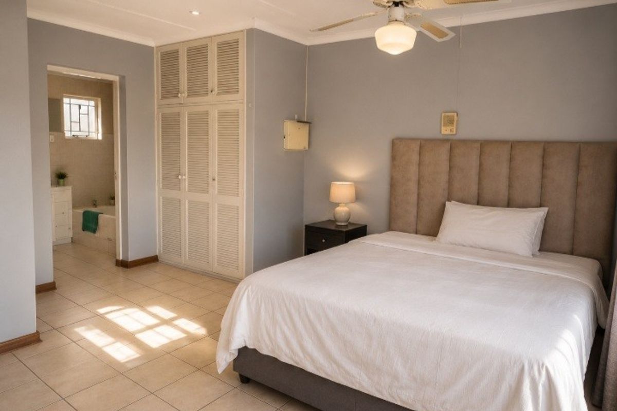 Spacious bedroom featuring tiled flooring, built-in cupboards, a ceiling fan, and direct access to an en-suite bathroom.