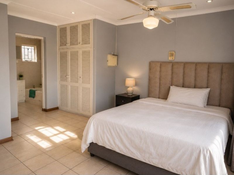 Spacious bedroom featuring tiled flooring, built-in cupboards, a ceiling fan, and direct access to an en-suite bathroom.