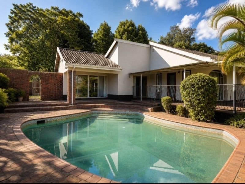 A rear exterior view featuring a swimming pool with brick paving, a covered patio area, and a brick boundary wall.