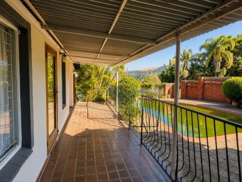 Covered patio area featuring tiled flooring and metal balustrades, overlooking a swimming pool and garden with scenic mountain views.