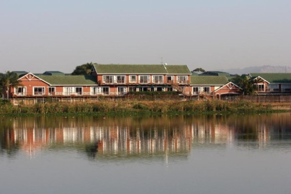 A scenic view of the rear elevation of the office building, featuring a multi-level brick structure with balconies overlooking a tranquil lake.
