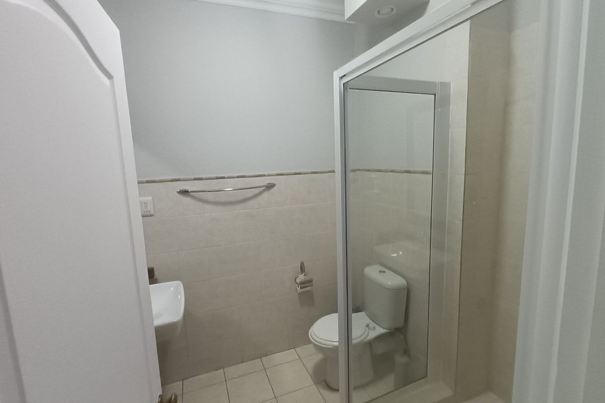 A clean, functional bathroom featuring a shower enclosure, wall-mounted basin, and neutral tiled finishes.