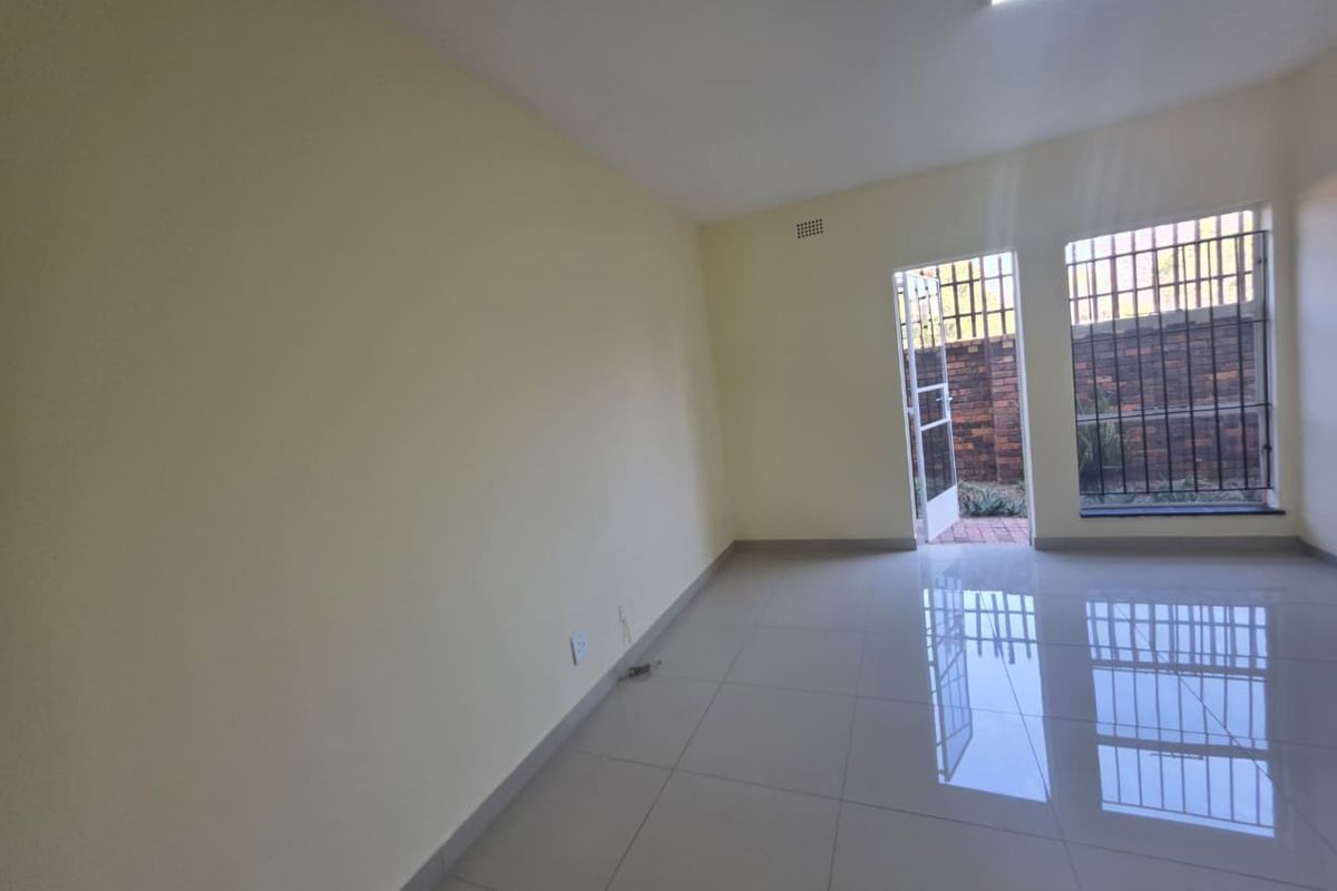 A bright, empty living area featuring polished tiled flooring, security bars on windows, and direct access to an outdoor space.