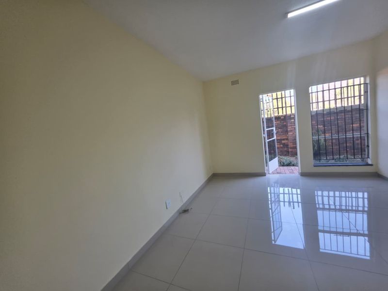 A bright, empty living area featuring polished tiled flooring, security bars on windows, and direct access to an outdoor space.