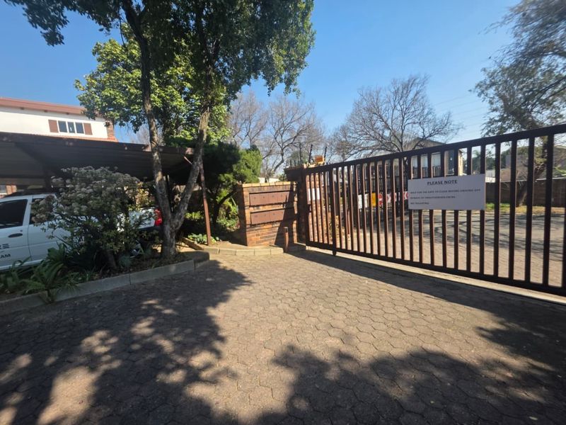 Front entrance of the commercial property featuring a secure metal gate, paved driveway, and covered carport parking area.