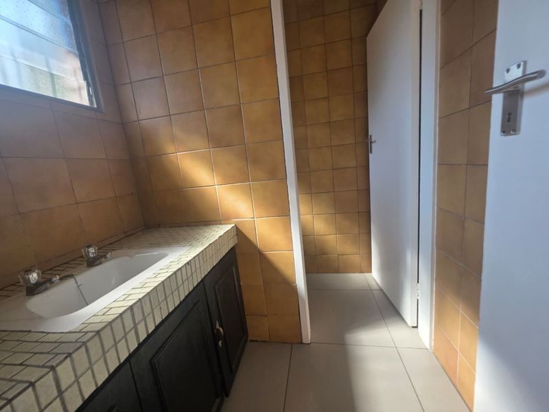 A functional bathroom featuring a built-in vanity with a basin and dated wall tiling, offering potential for a modern renovation.