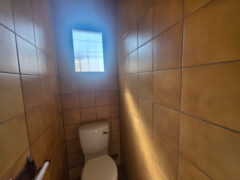 A compact, dated bathroom featuring full-height ceramic wall tiling, a standard toilet, and a safety grab rail.