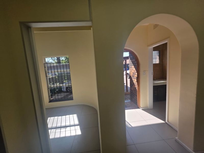 A bright, tiled hallway featuring arched architectural details, leading to an adjacent room and a secondary space with a built-in vanity.
