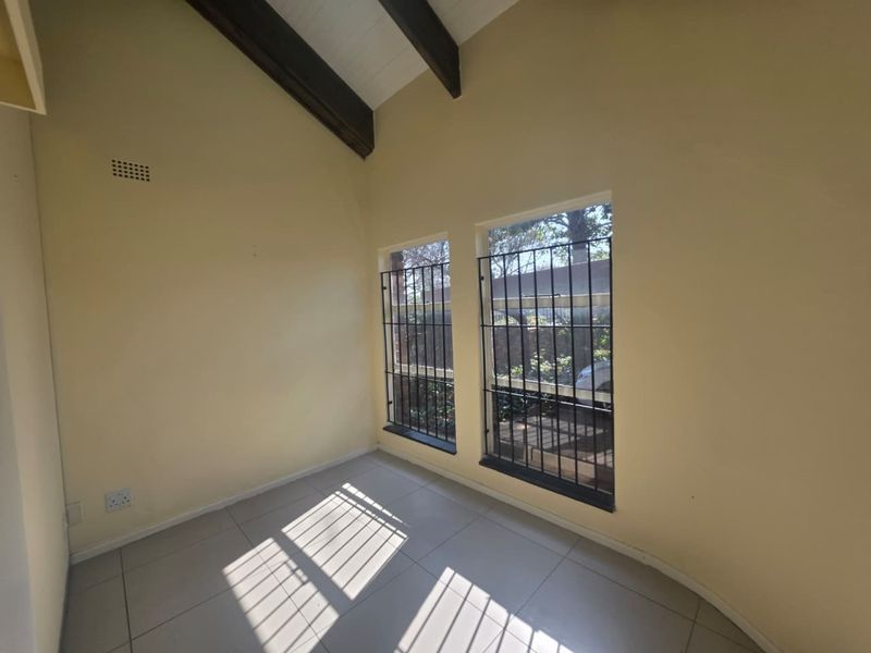 A bright, empty office space featuring tiled flooring, exposed timber ceiling beams, and windows fitted with security bars.