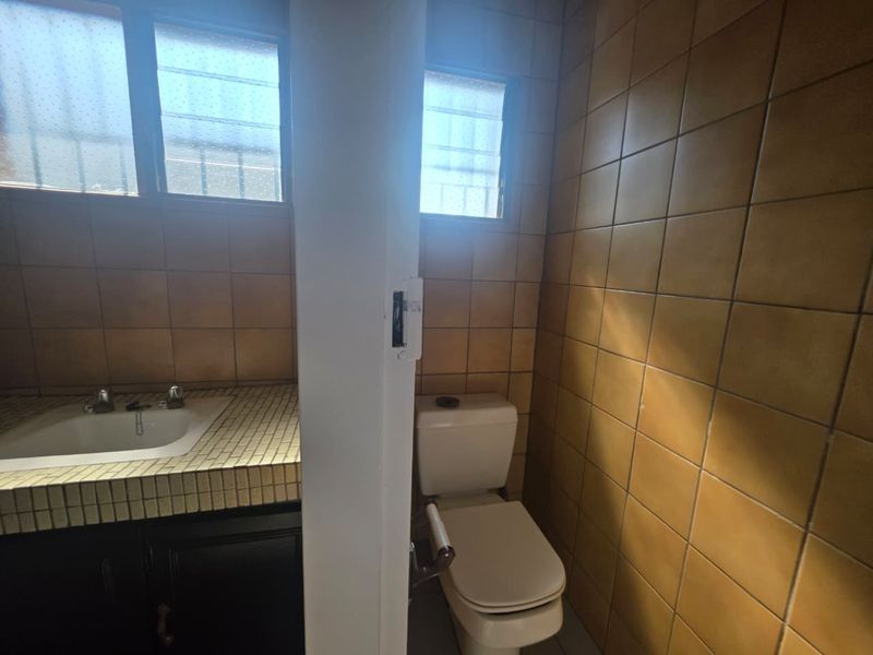 A functional bathroom featuring a tiled vanity with an inset basin and a separate toilet area with dated ceramic wall tiles.