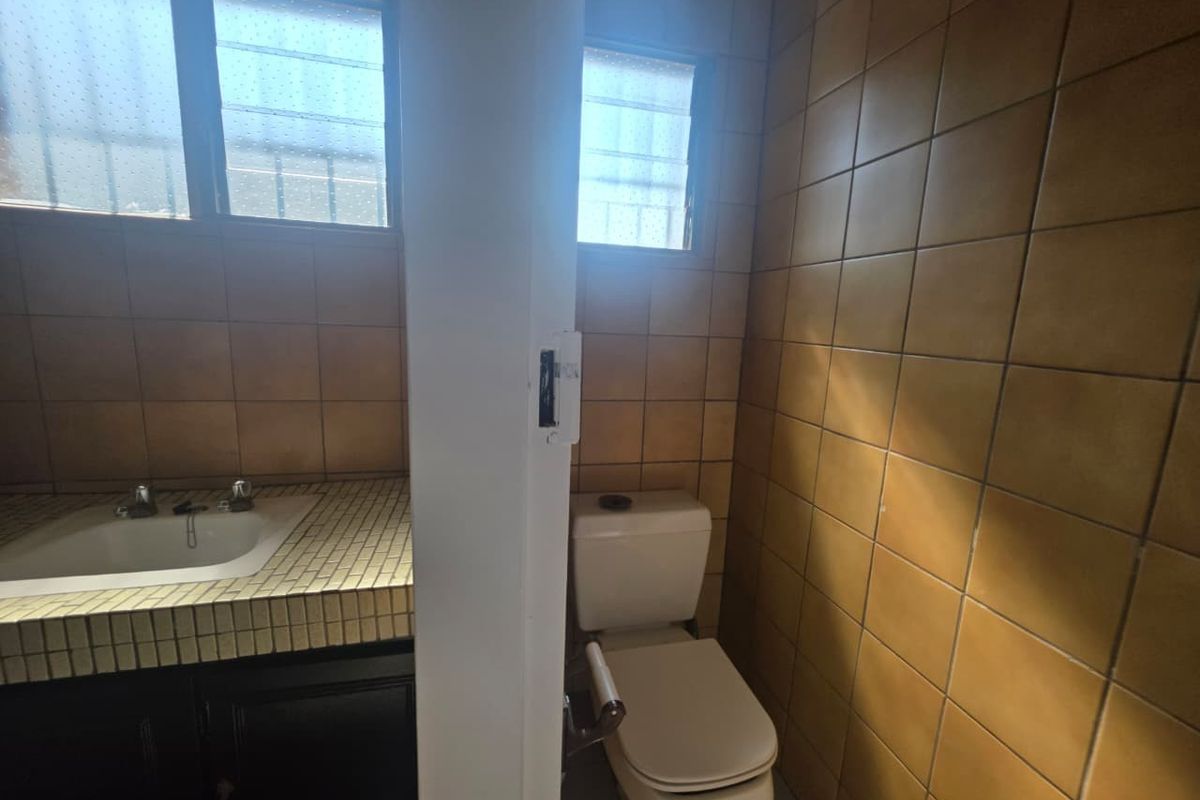 A functional bathroom featuring a tiled vanity with an inset basin and a separate toilet area with dated ceramic wall tiles.