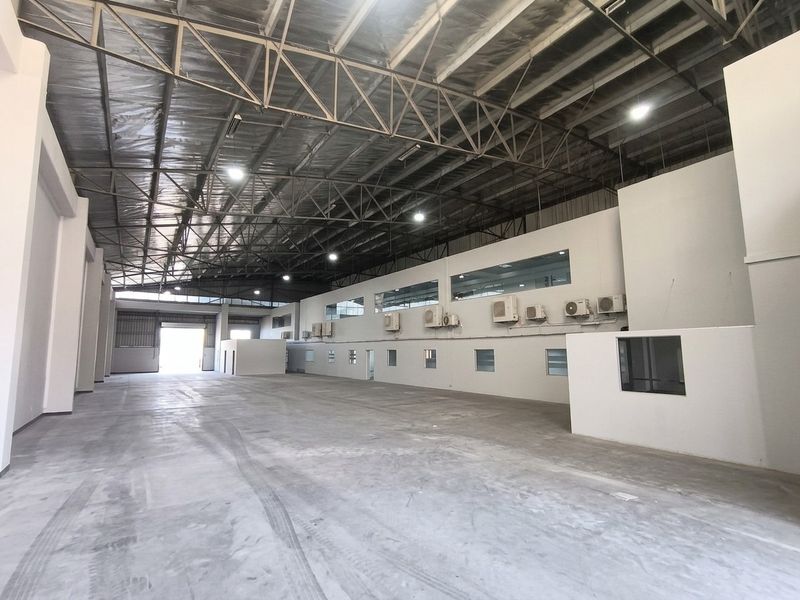 Spacious industrial warehouse featuring high ceilings with exposed steel trusses, polished concrete flooring, and integrated office spaces with wall-mounted air conditioning units.
