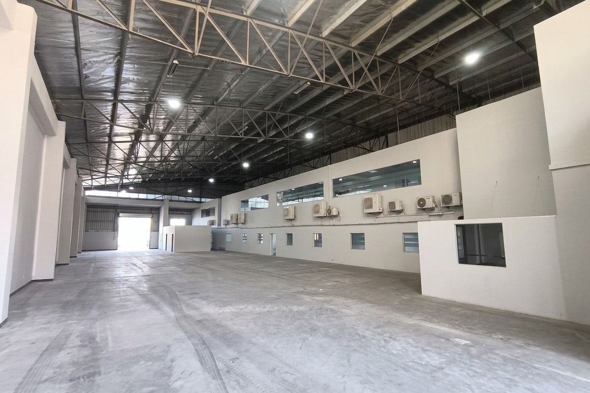 Spacious industrial warehouse featuring high ceilings with exposed steel trusses, polished concrete flooring, and integrated office spaces with wall-mounted air conditioning units.