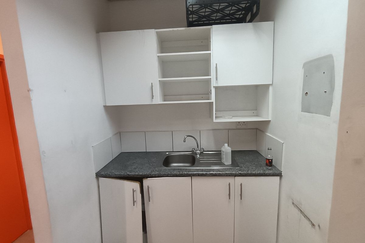 A compact kitchenette featuring white built-in cabinetry, a stainless steel sink, and tiled splashback, currently requiring minor repairs and maintenance.