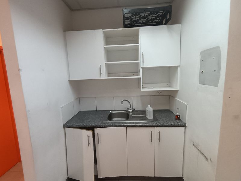 A compact kitchenette featuring white built-in cabinetry, a stainless steel sink, and tiled splashback, currently requiring minor repairs and maintenance.